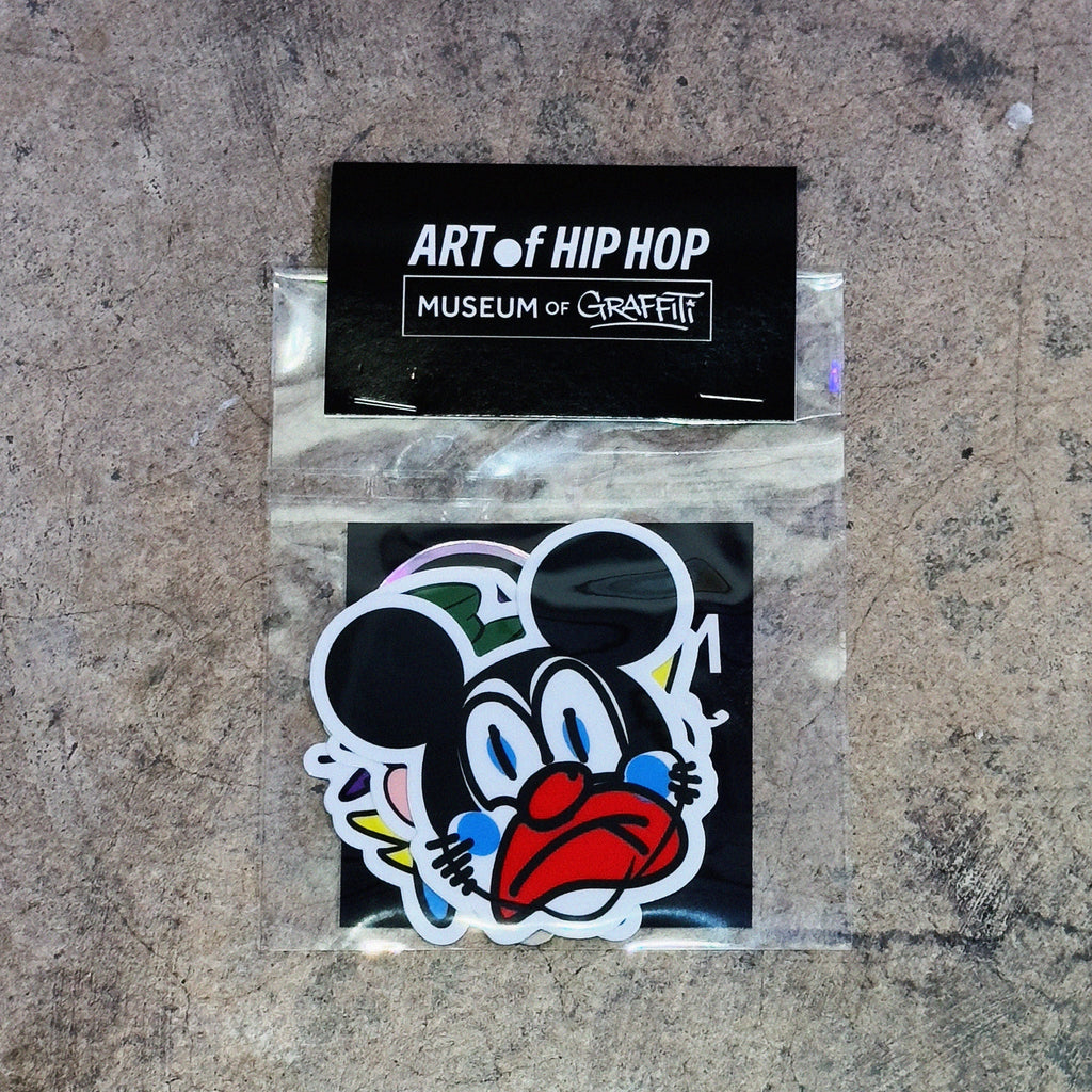A die-cut sticker featuring a stylized cartoon mouse face with black ears, blue eyes, and a red mouth, shown inside a clear plastic sleeve with a black backing card labeled 'ART of HIP HOP MUSEUM of CHICITY'.
